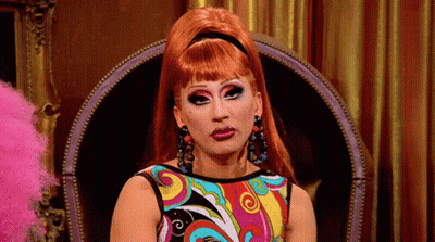 A Woman With Red Hair Is Sitting In A Chair Wearing A Colorful Dress . GIF