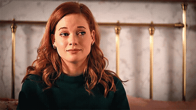 A Woman With Red Hair Is Sitting In Front Of A Bed . GIF