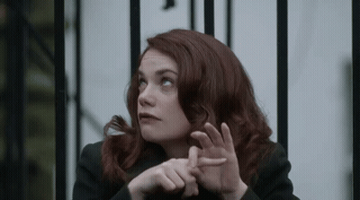 A Woman With Red Hair Is Sitting In Front Of A Metal Fence . GIF