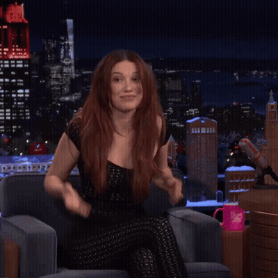 A Woman With Red Hair Is Sitting In Front Of A Microphone With A Pink Mug That Says I Love You On It GIF