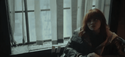 A Woman With Red Hair Is Sitting In Front Of A Window With Blinds . GIF