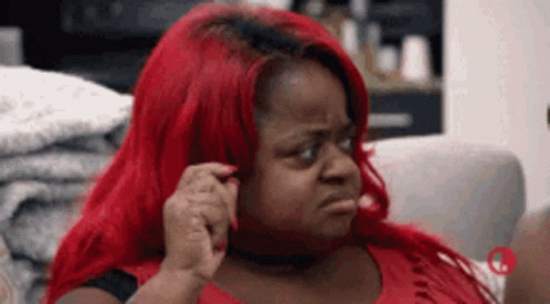 A Woman With Red Hair Is Sitting On A Couch And Making A Face . GIF