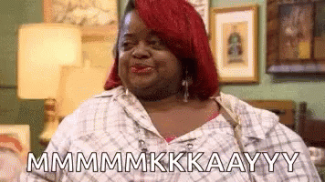A Woman With Red Hair Is Sitting On A Couch In A Living Room And Making A Funny Face . GIF
