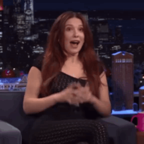 A Woman With Red Hair Is Sitting On A Couch With Her Mouth Open And Making A Funny Face . GIF