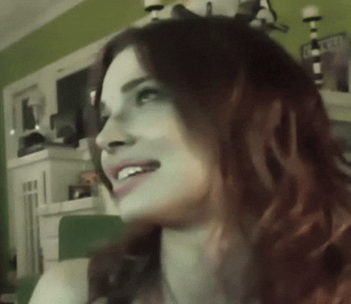 A Woman With Red Hair Is Smiling And Looking To The Side GIF