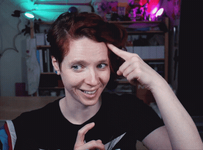 A Woman With Red Hair Is Smiling And Pointing At Her Head GIF