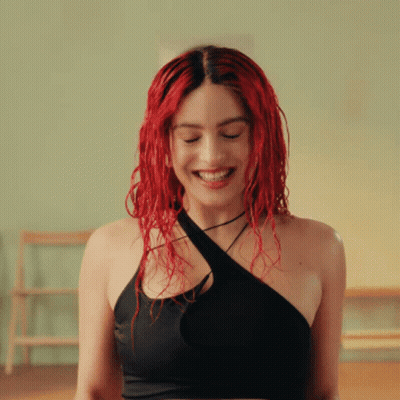 A Woman With Red Hair Is Smiling In A Black Top GIF