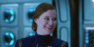 A Woman With Red Hair Is Smiling In Front Of A Wall With Blue Lights GIF