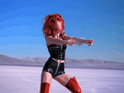 A Woman With Red Hair Is Standing In A Desert GIF