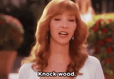 A Woman With Red Hair Is Standing In Front Of A Bush And Says `` Knock Wood '' . GIF