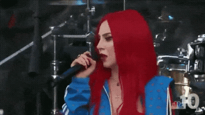 A Woman With Red Hair Is Standing In Front Of A Drum Set And Looking At The Camera . GIF