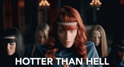 A Woman With Red Hair Is Standing In Front Of A Group Of Women With The Words `` Hotter Than Hell '' Written On The Bott GIF