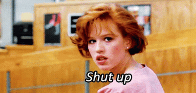A Woman With Red Hair Is Standing In Front Of A Wooden Wall And Saying Shut Up . GIF