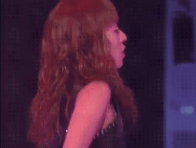 A Woman With Red Hair Is Standing On A Stage In Front Of A Crowd . GIF