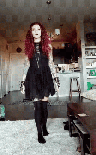 A Woman With Red Hair Is Wearing A Black Dress And Black Socks GIF