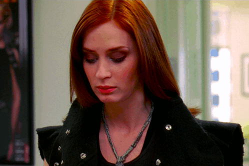 A Woman With Red Hair Is Wearing A Black Jacket And Necklace GIF
