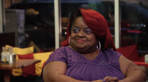 A Woman With Red Hair Is Wearing A Purple Shirt And Pearl Earrings GIF