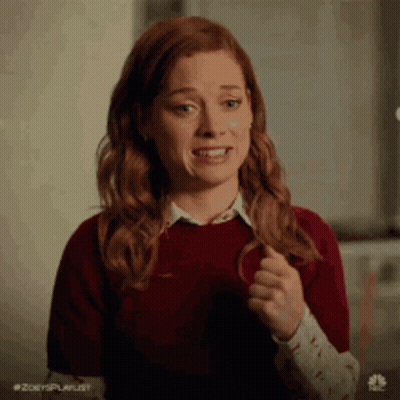 A Woman With Red Hair Is Wearing A Red Sweater And A White Shirt And Is Making A Funny Face . GIF