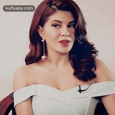 A Woman With Red Hair Is Wearing A White Dress And Earrings . GIF