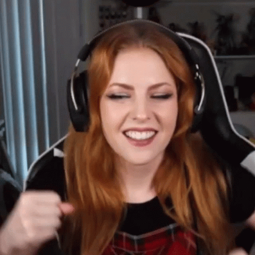 A Woman With Red Hair Is Wearing Headphones And Smiling While Sitting In A Chair . GIF