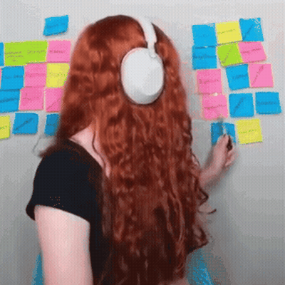 A Woman With Red Hair Is Wearing Headphones And Writing On Sticky Notes GIF