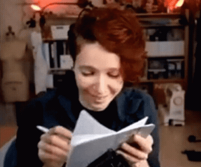 A Woman With Red Hair Is Writing On A Piece Of Paper While Holding A Pen . GIF