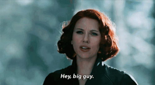 A Woman With Red Hair Says Hey Big Guy In Front Of A Blue Background GIF