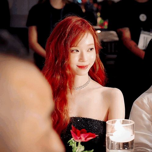 A Woman With Red Hair Sits At A Table With A Glass Of Water And A Flower GIF