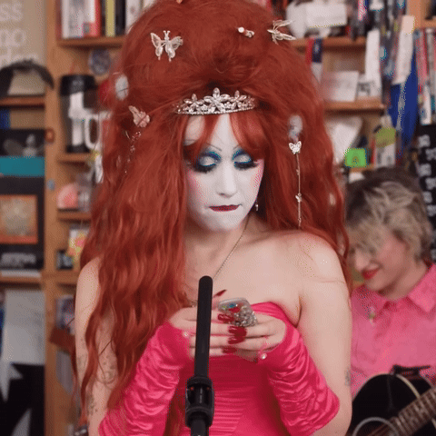 A Woman With Red Hair Wearing A Pink Dress And Gloves GIF