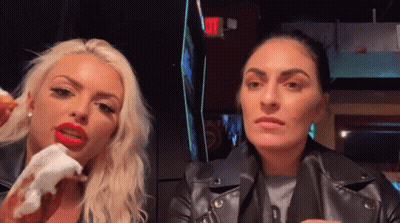 A Woman With Red Lips Is Eating A Donut Next To Another Woman In A Black Leather Jacket GIF