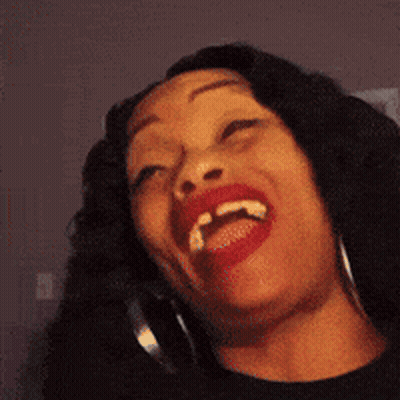 A Woman With Red Lipstick And Hoop Earrings Is Laughing With Her Mouth Open GIF