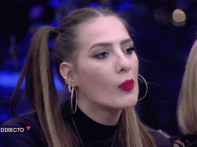 A Woman With Red Lipstick And Hoop Earrings Is Making A Face In Front Of A Directo Sign GIF