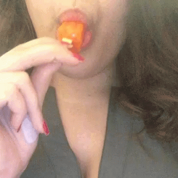 A Woman With Red Nails Is Eating A Piece Of Orange Candy . GIF