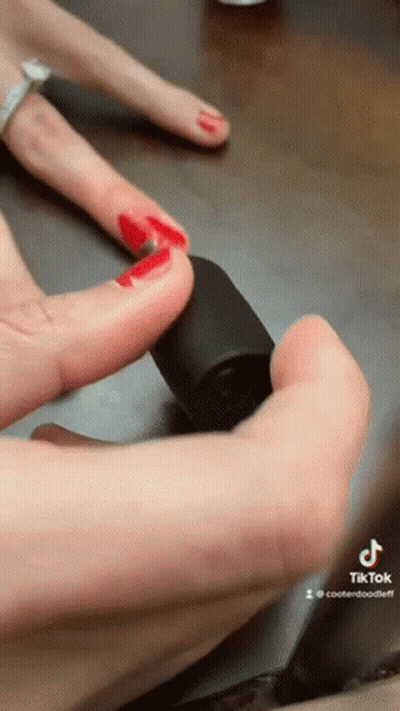 A Woman With Red Nails Is Holding A Bottle Of Nail Polish In Her Hand GIF