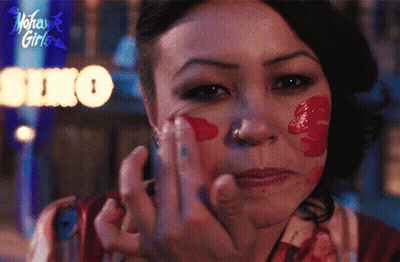 A Woman With Red Paint On Her Face Has A Sign Behind Her That Says Soho GIF