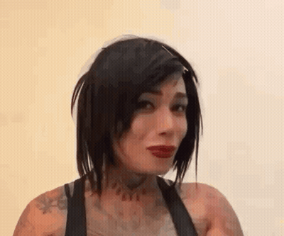 A Woman With Short Black Hair And Red Lipstick Is Smiling And Looking At The Camera . GIF