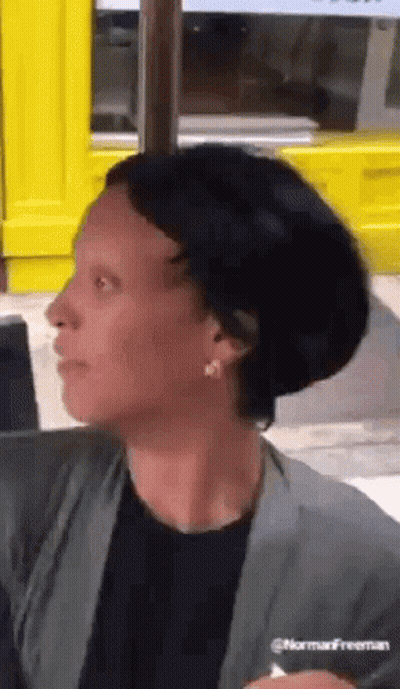 A Woman With Short Black Hair Is Sitting In Front Of A Yellow Door . GIF