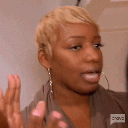 A Woman With Short Blonde Hair And Hoop Earrings Is Making A Face . GIF