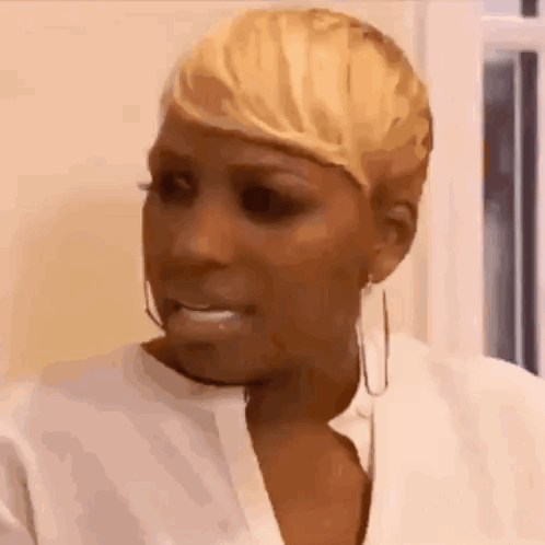 A Woman With Short Blonde Hair And Hoop Earrings Is Making A Funny Face . GIF