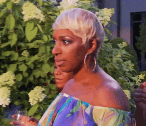 A Woman With Short Blonde Hair Is Holding A Glass Of Wine In Her Hand . GIF