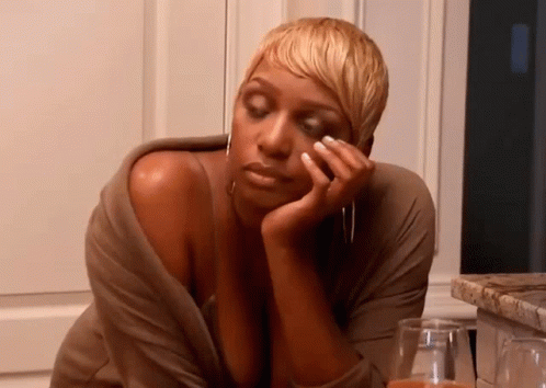 A Woman With Short Blonde Hair Is Sitting At A Table With Her Hand On Her Face GIF
