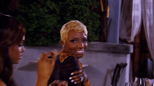 A Woman With Short Blonde Hair Is Smiling While Holding A Glass GIF