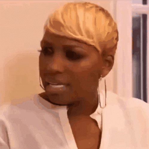 A Woman With Short Blonde Hair Is Wearing A White Shirt And Earrings And Making A Funny Face . GIF