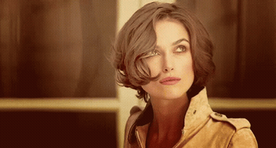 A Woman With Short Brown Hair Is Wearing A Brown Jacket And Looking Up . GIF