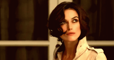 A Woman With Short Brown Hair Is Wearing A Tan Jacket GIF