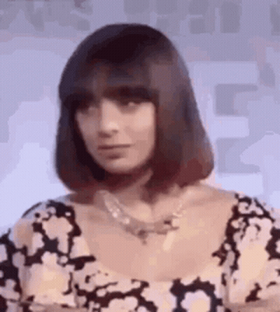 A Woman With Short Hair And A Necklace Is Wearing A Black And White Dress . GIF