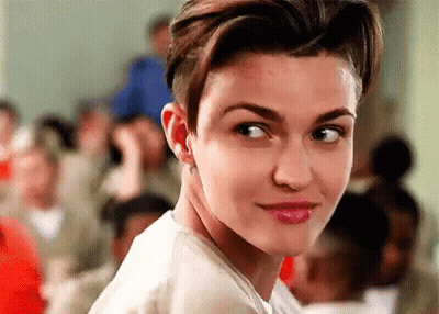 A Woman With Short Hair And A Shaved Head Is Looking At The Camera In Front Of A Crowd Of People . GIF