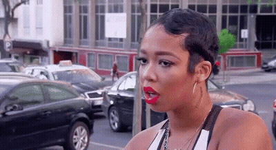A Woman With Short Hair And Red Lipstick Is Standing On A Street . GIF