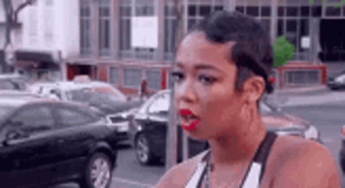 A Woman With Short Hair And Red Lipstick Is Standing On A Street In Front Of A Parking Meter . GIF