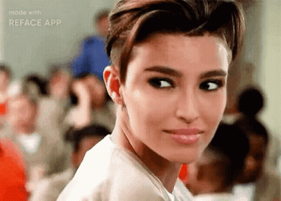 A Woman With Short Hair Is Looking At The Camera In Front Of A Crowd . GIF